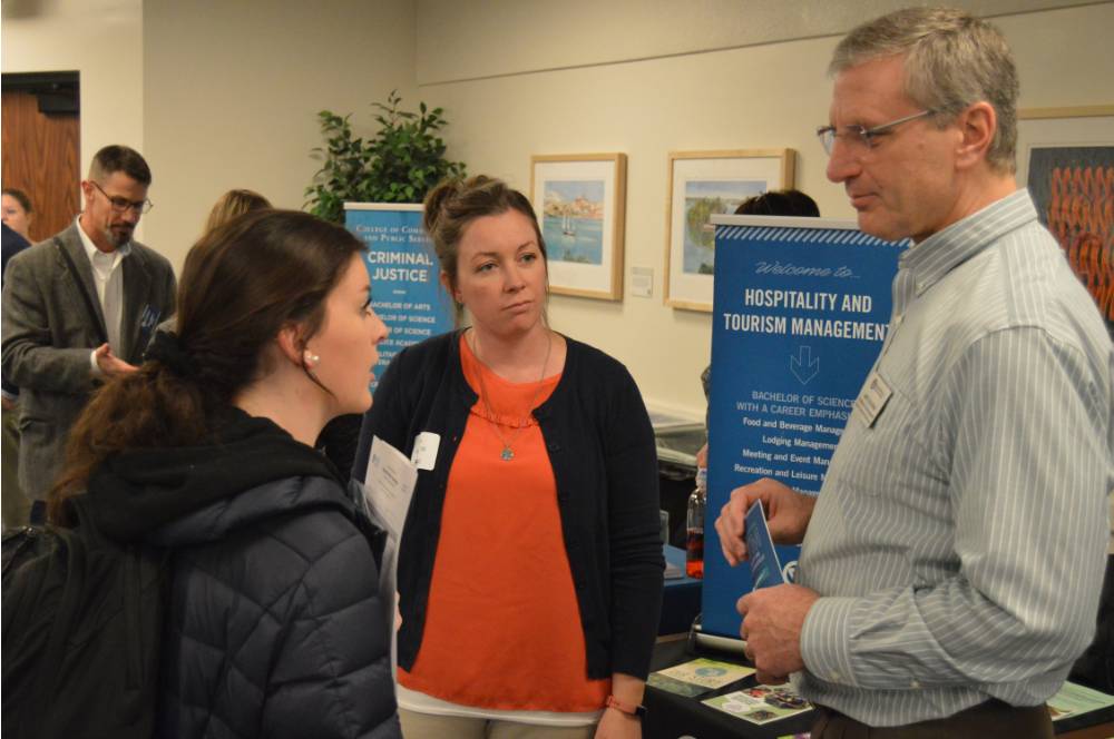 Student, alumna and faculty talking to one another at the Academic Major Fair.
